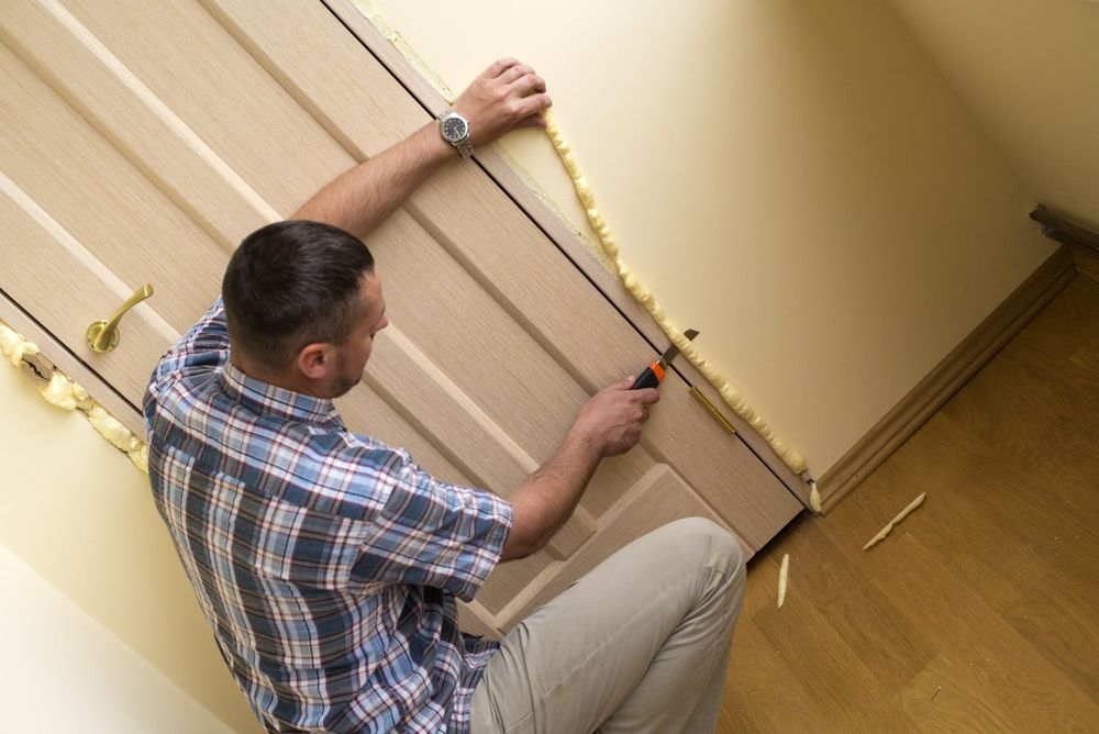 Man trimming foam insulation from around a door frame