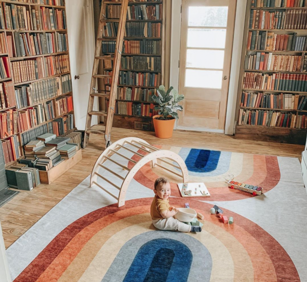 baby sitting on a rainbow rug in a play room