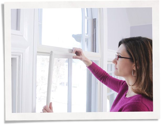 A person is installing a window insert into their window. They are wearing a purple sweater, hoop earrings and brown glasses.