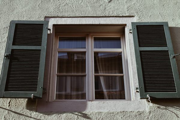 Two green shutters are on each side of a window.