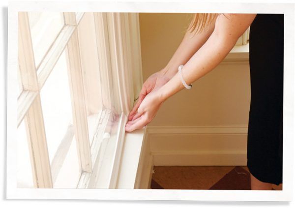 A close-up image of a person installing window inserts. They are wearing a black dress and have a clear bracelet on their left wrist. 