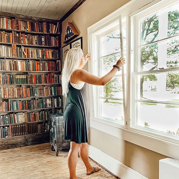 woman next to large bookshelf installing Indow window insert: sound-absorbing vs sound-blocking