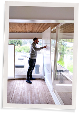 A person is installing a large window insert while wearing a grey sweater and dark pants.
