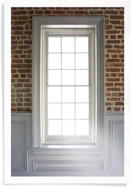 Tall, vertical window framed with old, red brick and white paneling, with a window insert inside the frame.