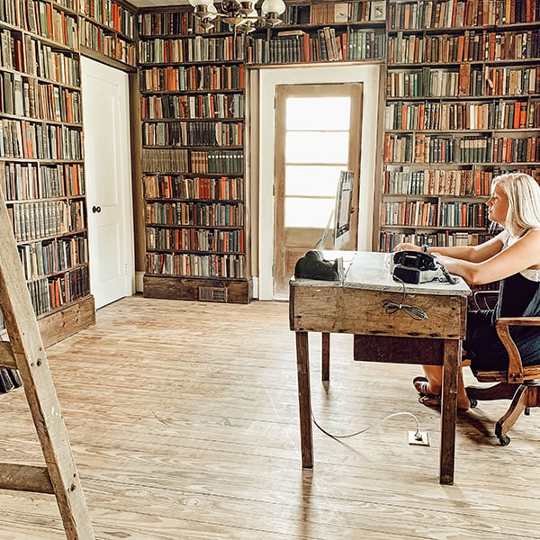 woman at desk in her home library with floor to ceiling bookshelves