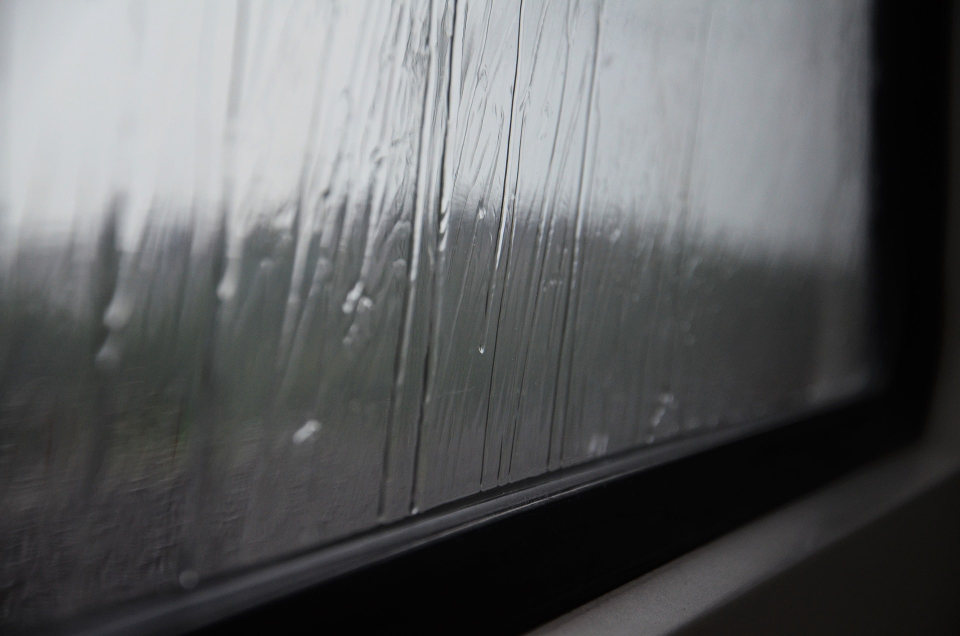 A close-up of raindrops dripping down the bottom of a window.